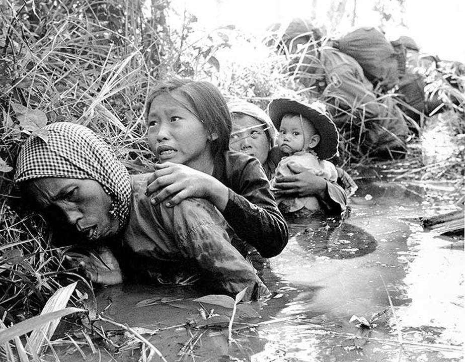 Women and children crouch in a muddy canal as they take cover from intense Viet Cong fire at Bao Trai, about 20 miles west of Saigon.